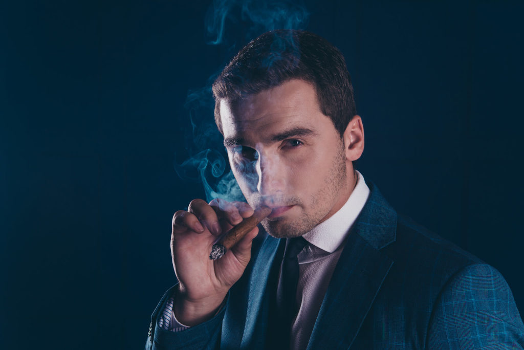 A smartly dressed man enjoys a lit cigar.