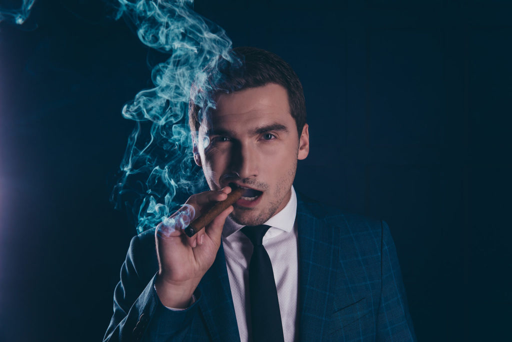 A smartly dressed man enjoys a lit cigar.